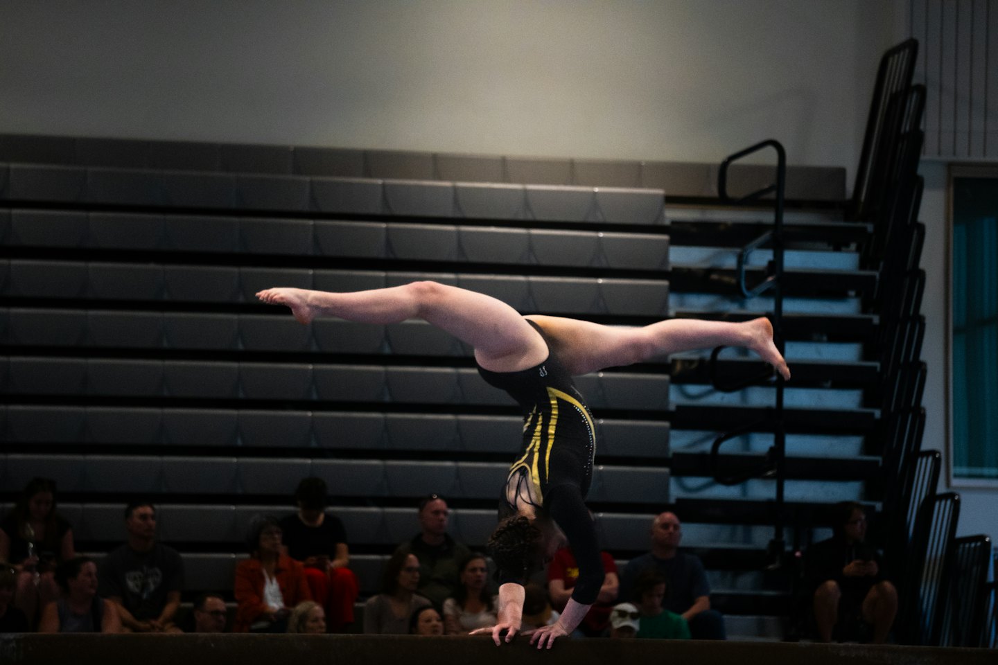 Gymnast performs a handstand split on a balance beam.